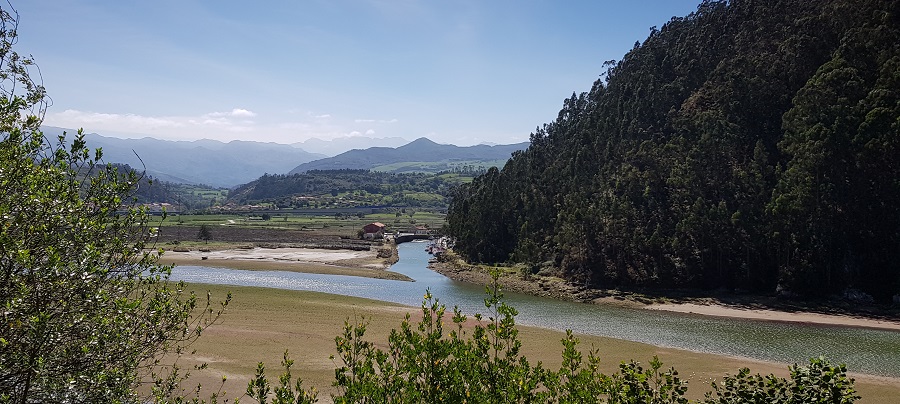 Ría de Tina Mayor y Caño del Mazo, con la Cofradía de Pescadores de Bustio y los Picos de Europa de fondo, desde la carretera de Pechón